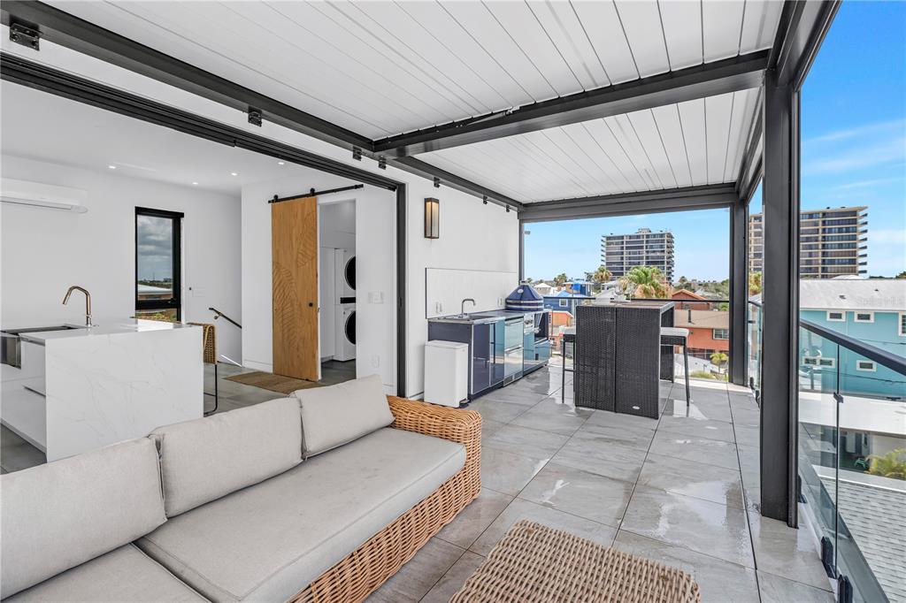 A modern indoor-outdoor living space features a wicker sectional, kitchen island, and folding glass doors — 30 80TH AVENUE, TREASURE ISLAND, FL
