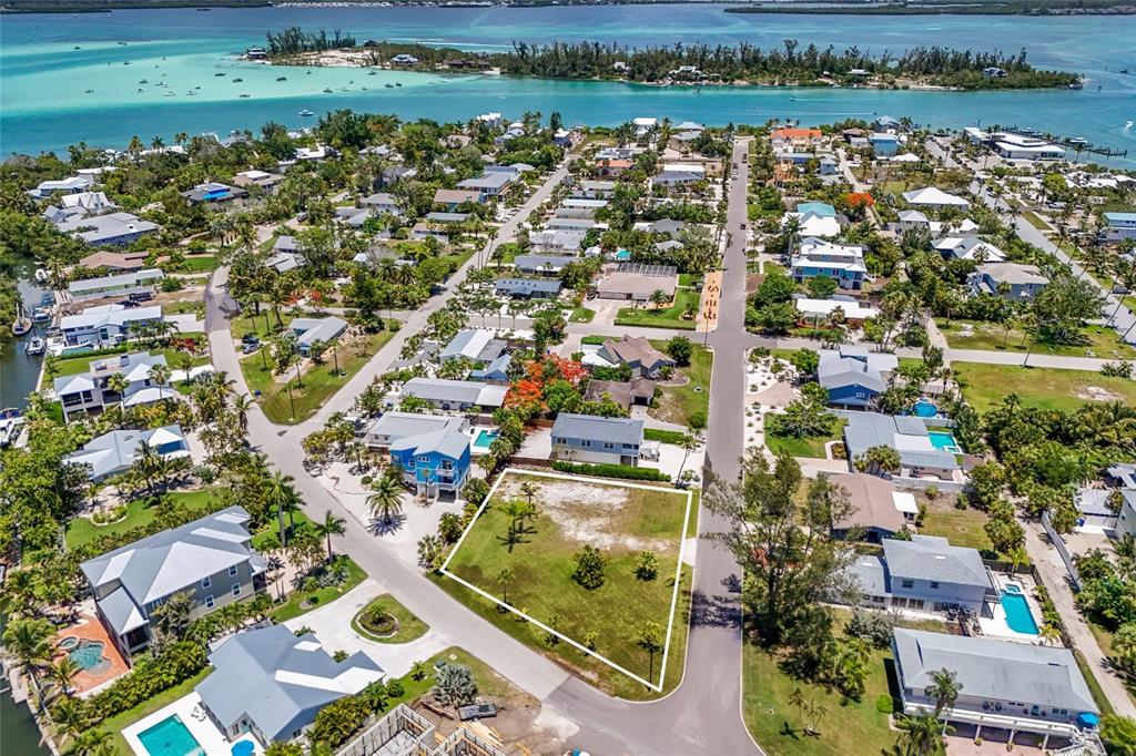 An aerial view shows a vacant residential lot outlined in white within a coastal neighborhood — 591 RUSSELL STREET, LONGBOAT KEY, FL
