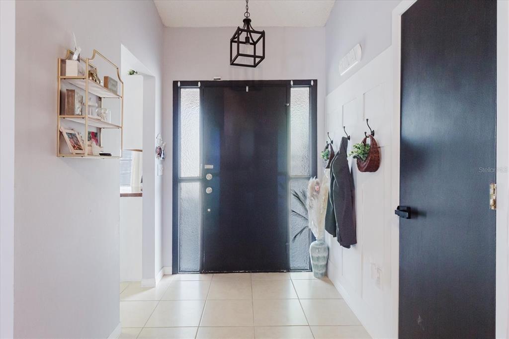 A bright entryway features a black front door, tile flooring, and white paneled walls — 2427 COMERWOOD DRIVE, SPRING HILL, FL