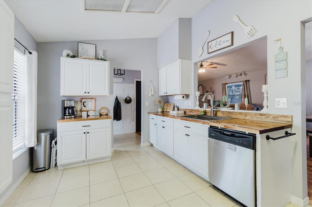 A kitchen with white cabinets, wood countertops, tile flooring, and a pass-through window — 2427 COMERWOOD DRIVE, SPRING HILL, FL