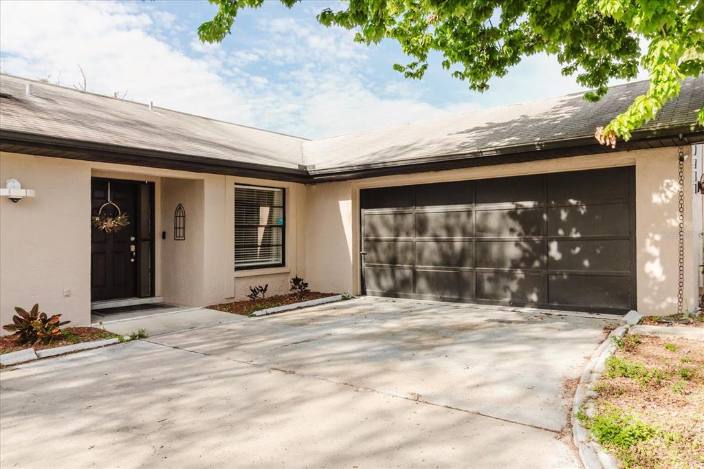 A single-story house exterior features a beige stucco facade, a dark garage door, and a front entrance — 2427 COMERWOOD DRIVE, SPRING HILL, FL