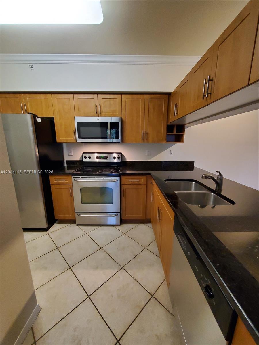 A kitchen features wood cabinets, stainless steel appliances, and dark countertops over tiled floors — 6458 Emerald Dunes # 304, West Palm Beach FL 33411, WEST PALM BEACH, FL
