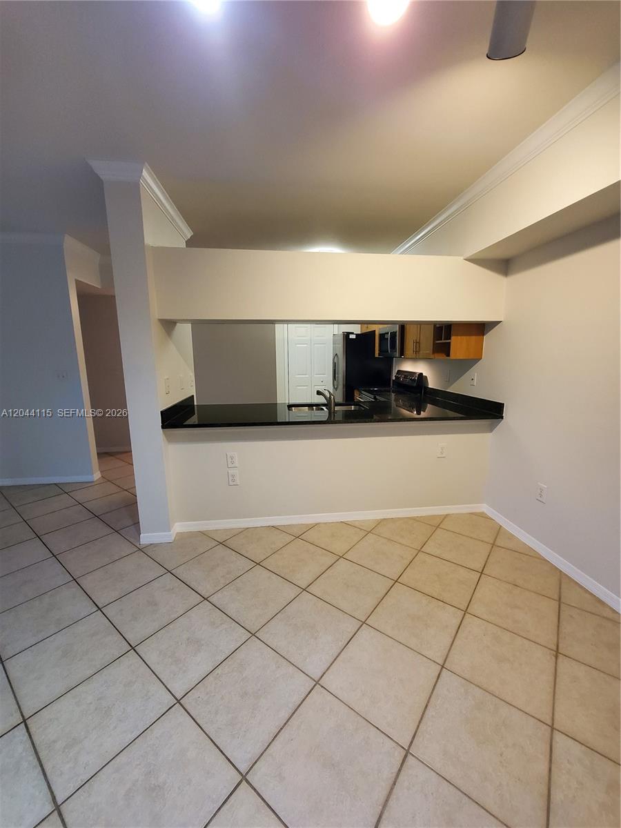 A kitchen with black countertops and wooden cabinets overlooks a tiled dining area — 6458 Emerald Dunes # 304, West Palm Beach FL 33411, WEST PALM BEACH, FL