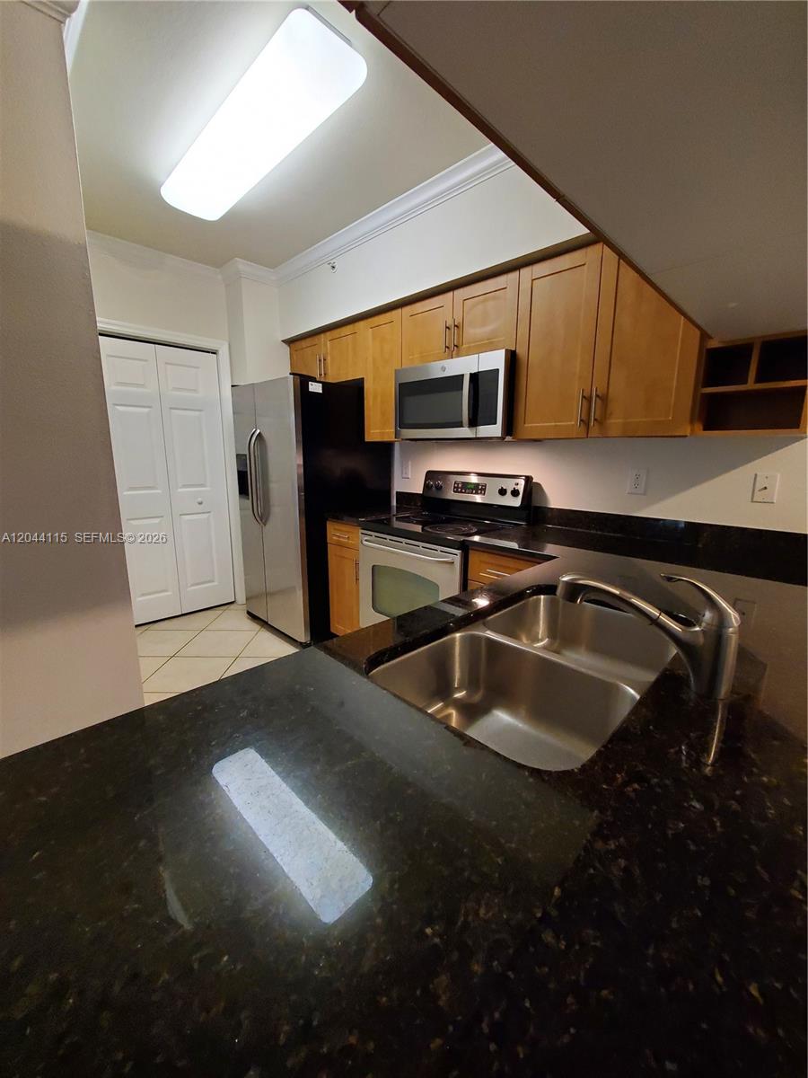 A kitchen features dark granite countertops, stainless steel appliances, and light wood cabinetry — 6458 Emerald Dunes # 304, West Palm Beach FL 33411, WEST PALM BEACH, FL
