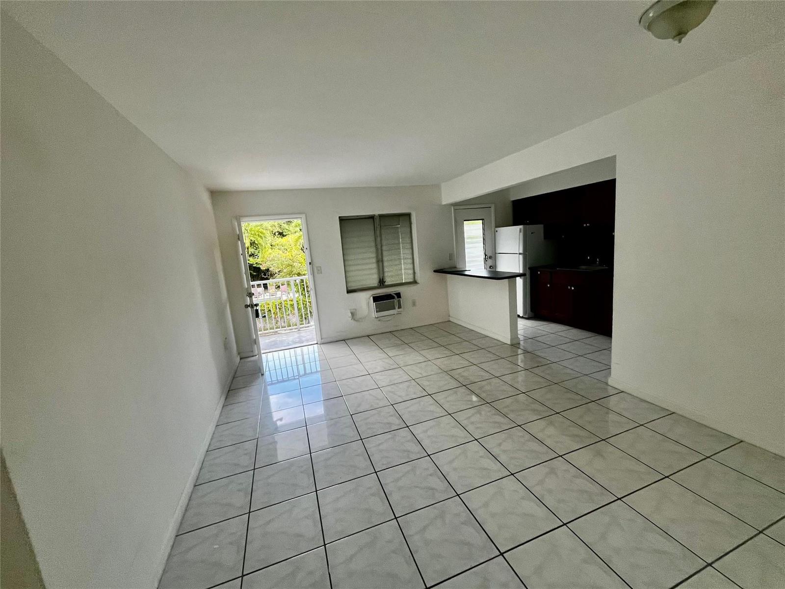 An open-concept living area with white tile floors, a kitchen pass-through, and a balcony door — 751 NE 83rd Terrace # 18, Miami FL 33138, MIAMI, FL