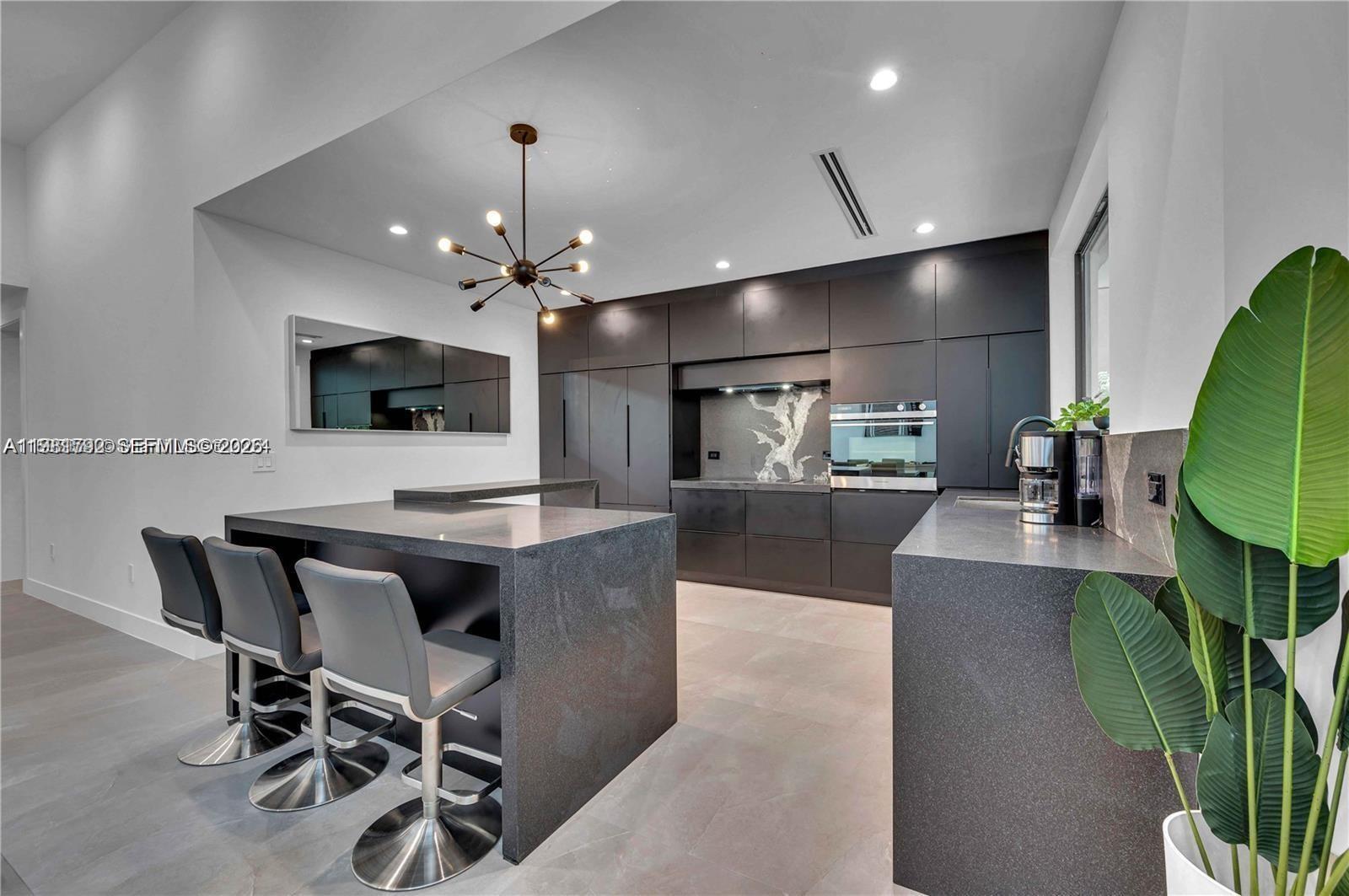 A modern kitchen features dark cabinetry, a matching island with bar stools, and stone countertops — 155 NW 51st St # 0, Miami FL 33127, MIAMI, FL