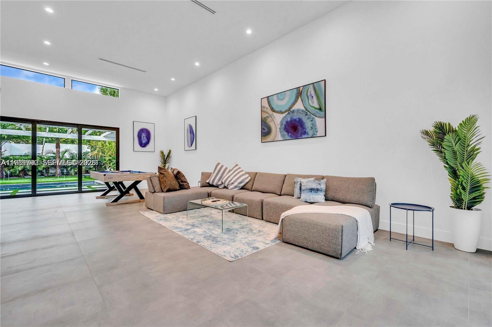 A modern living room features a large gray sectional sofa, a glass coffee table, and artwork — 155 NW 51st St # 0, Miami FL 33127, MIAMI, FL