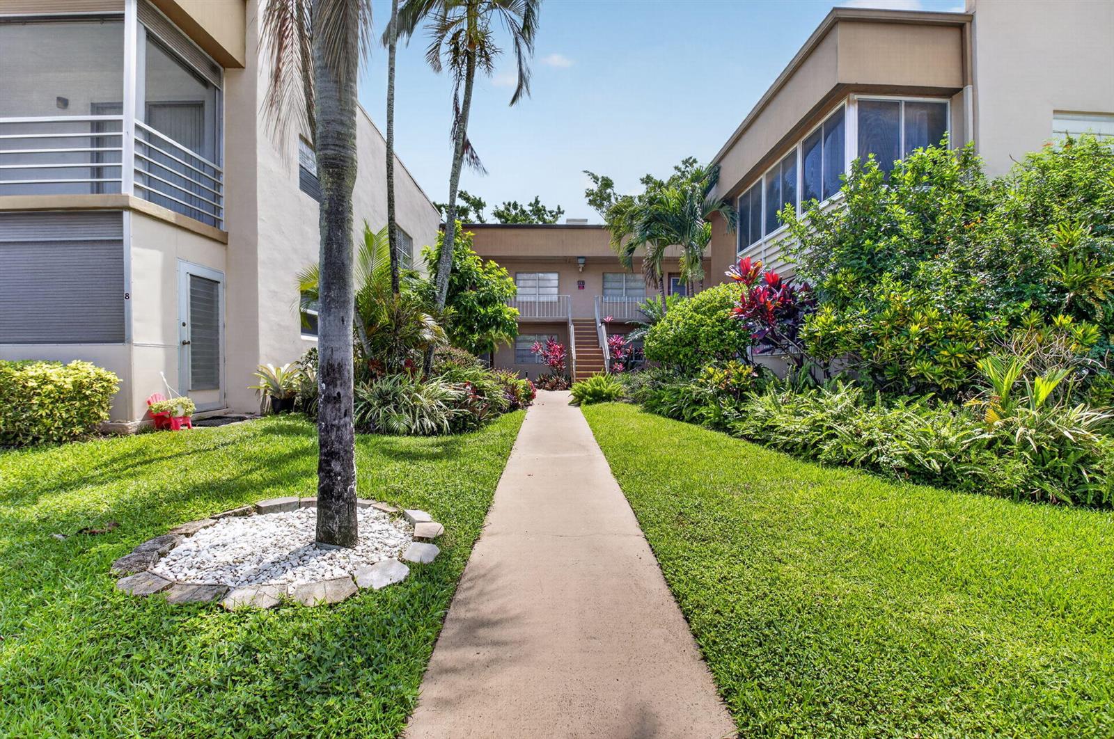 A concrete walkway leads between two apartment buildings surrounded by lush tropical landscaping and lawns — 14 Flanders # A, Delray Beach FL 33484, DELRAY BEACH, FL