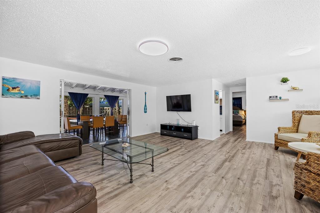 A living room with wood-look flooring, a leather sectional, a glass coffee table, and patio access — 4055 BAY OAKS CIRCLE, ENGLEWOOD, FL