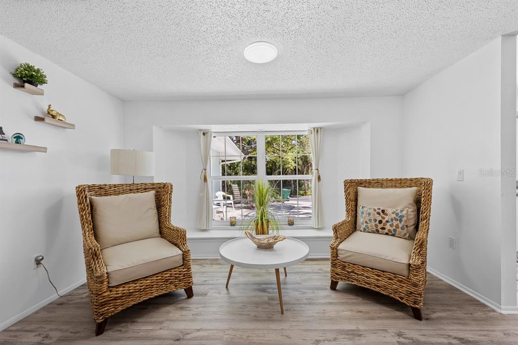 A bright room features two wicker armchairs, a round coffee table, and a bay window — 4055 BAY OAKS CIRCLE, ENGLEWOOD, FL