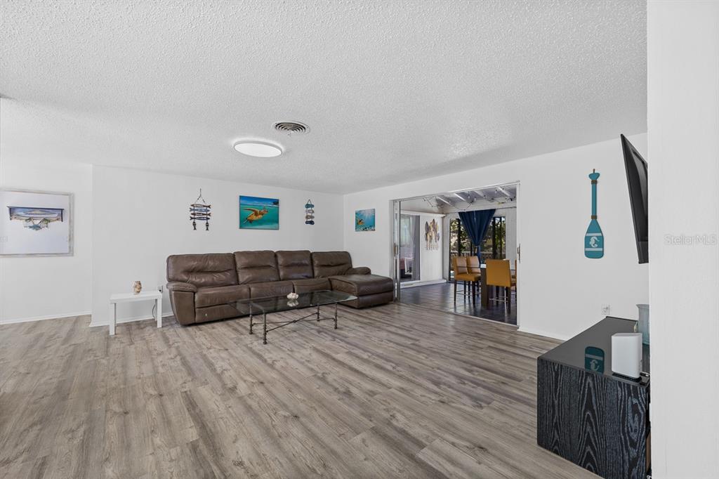 A living room with wood-look flooring, a brown leather sectional, and a glass coffee table — 4055 BAY OAKS CIRCLE, ENGLEWOOD, FL