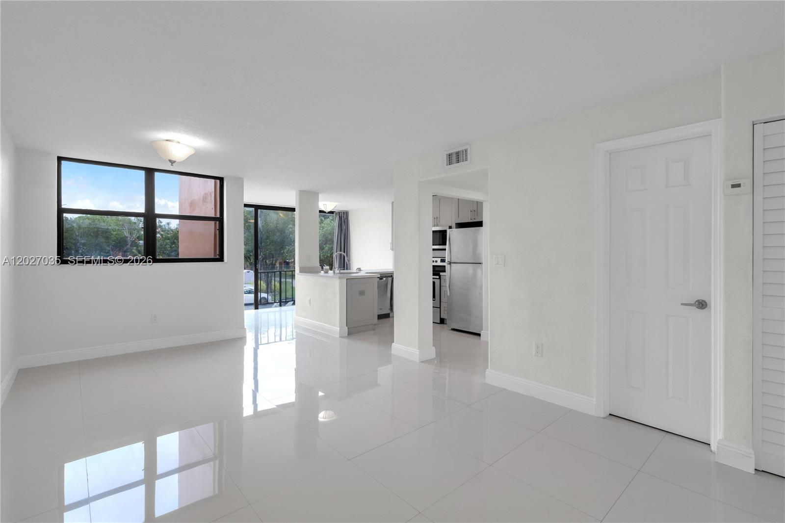 A bright, open-concept living area features white tile flooring, a kitchen, and a balcony view — 9440 W Flagler St # 208, Miami FL 33174, MIAMI, FL