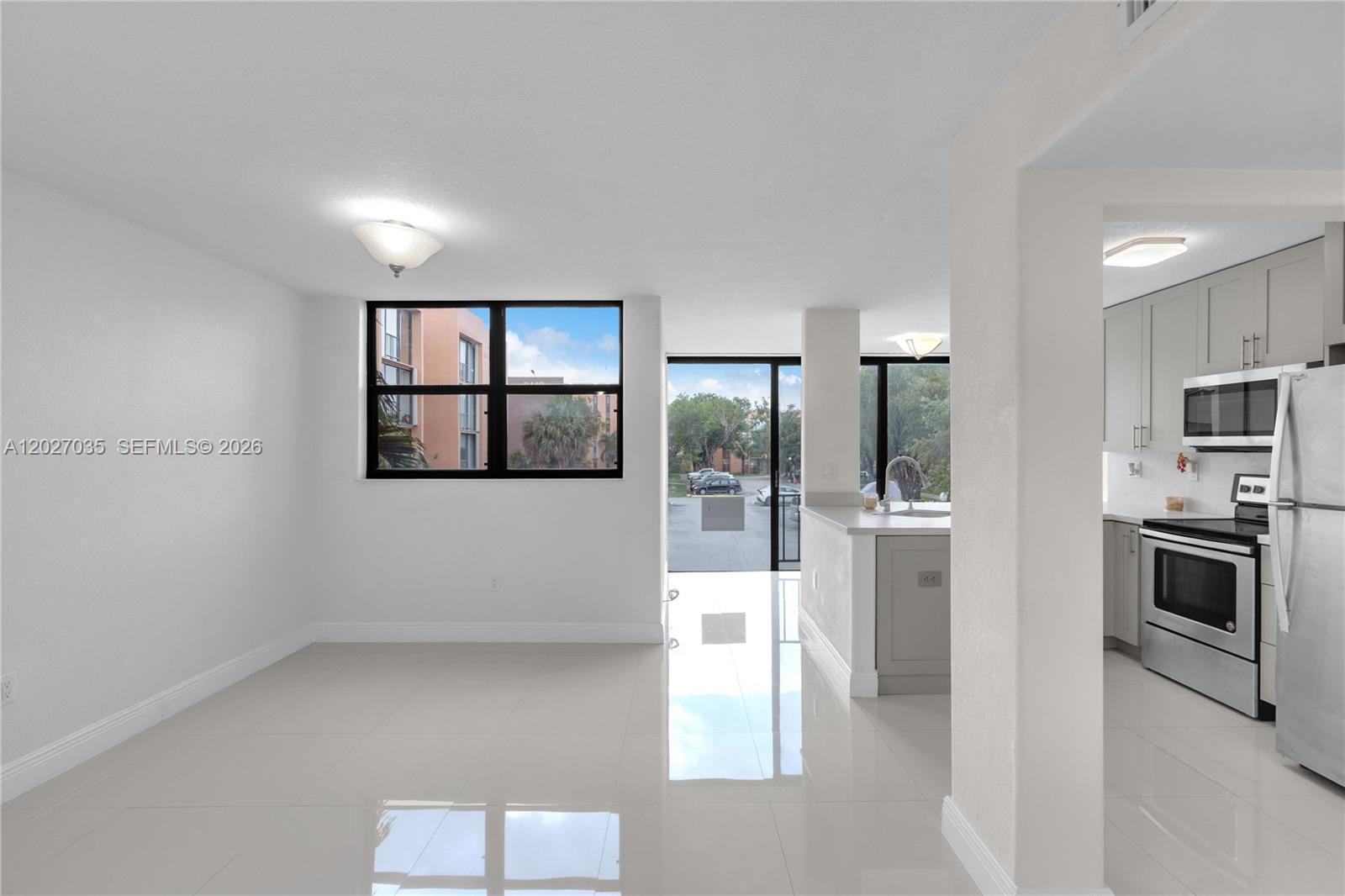 A bright, open-concept living area features white tile floors, a kitchen, and a glass door — 9440 W Flagler St # 208, Miami FL 33174, MIAMI, FL