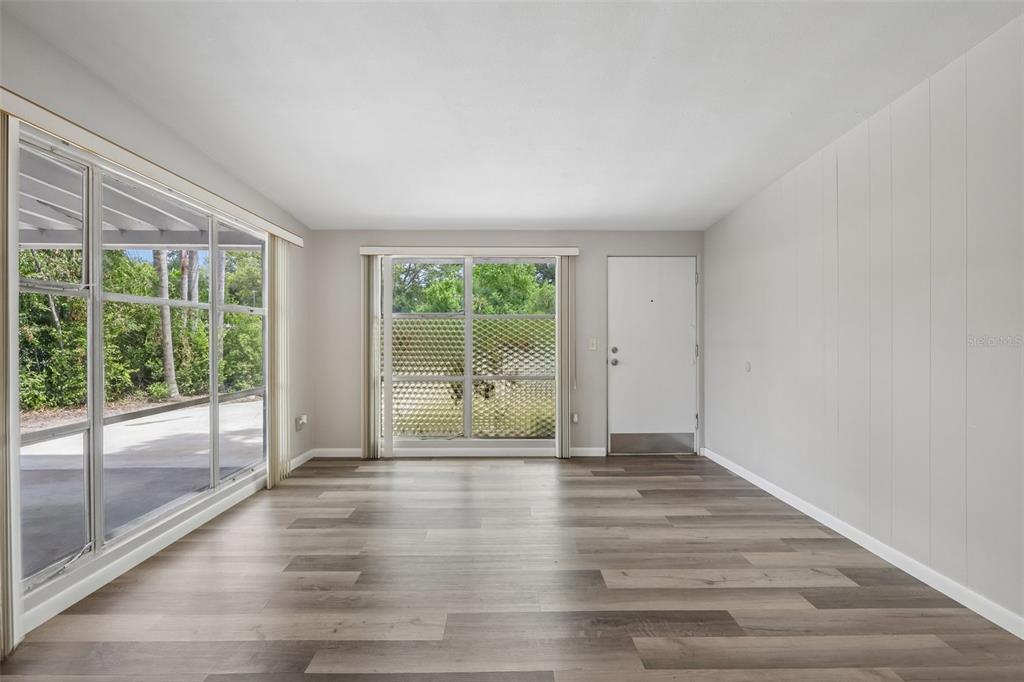An empty room with wood-look flooring, large windows, and a white entry door — 2117 BARCELONA DRIVE, CLEARWATER, FL