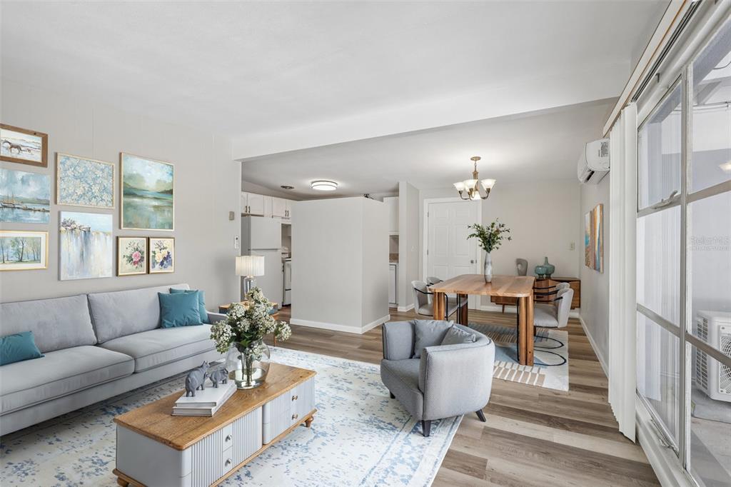 A living room and dining area with light wood floors, a grey sofa, and artwork — 2117 BARCELONA DRIVE, CLEARWATER, FL