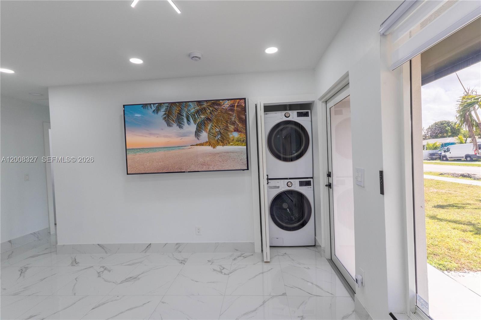 A room with white walls, marble-look tile flooring, a wall-mounted television, and a stacked laundry unit — 3001 SW 35th Ave, West Park FL 33023, WEST PARK, FL