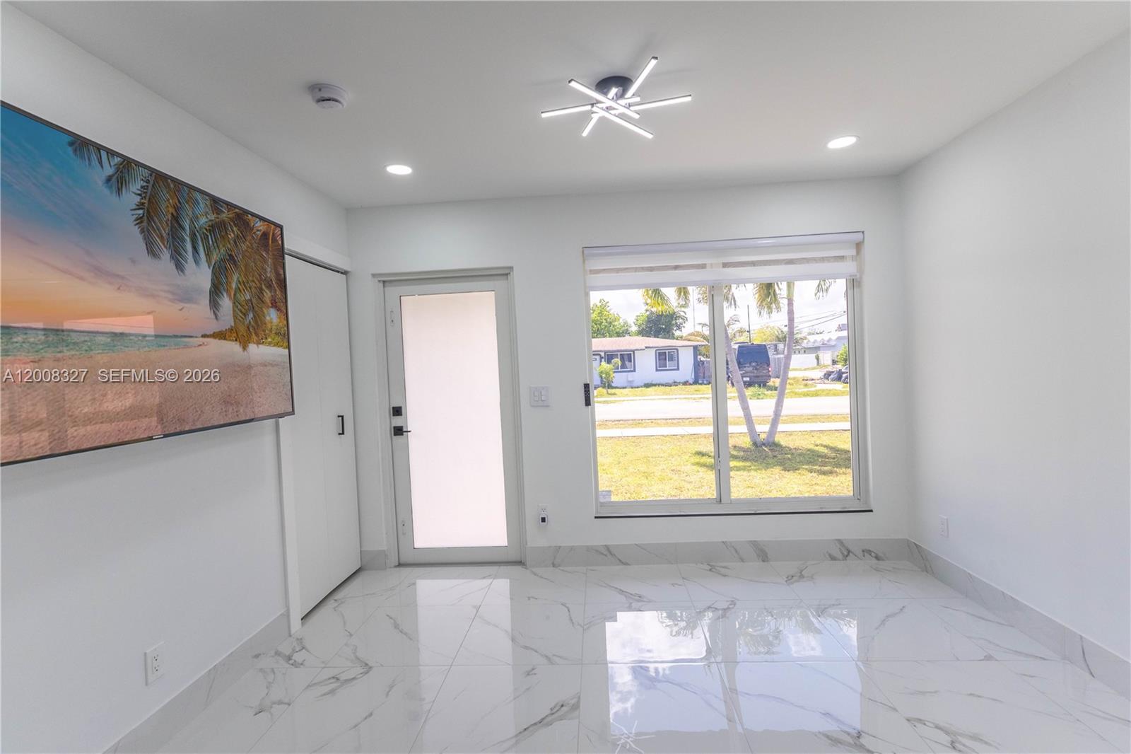 A bright room features white marble-look tile flooring, a modern ceiling light, and a window — 3001 SW 35th Ave, West Park FL 33023, WEST PARK, FL