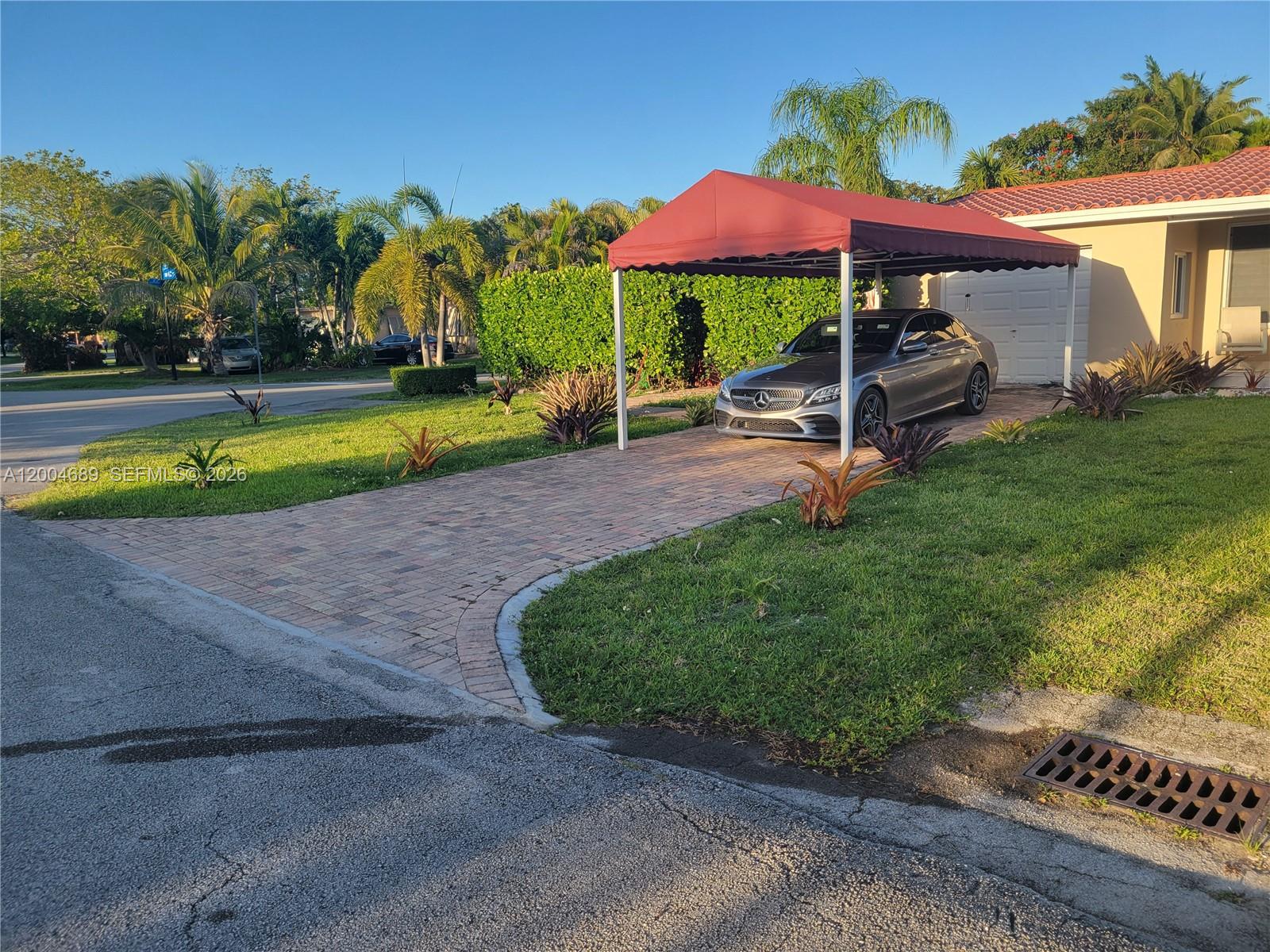 A gray car is parked under a red canopy on a brick driveway — SOUTH MIAMI, FL