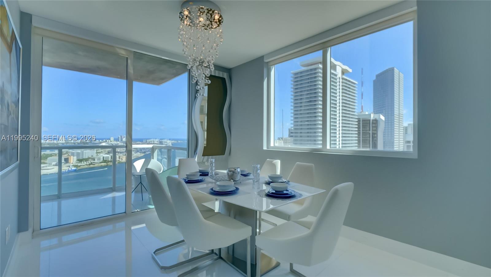 A modern dining room features a white table, white chairs, a crystal chandelier, and floor-to-ceiling windows — 253 NE 2nd St # 3509, Miami FL 33132, MIAMI, FL