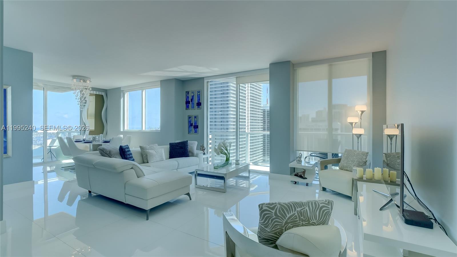 A bright, modern living room features white tile floors, a sectional sofa, and floor-to-ceiling windows — 253 NE 2nd St # 3509, Miami FL 33132, MIAMI, FL