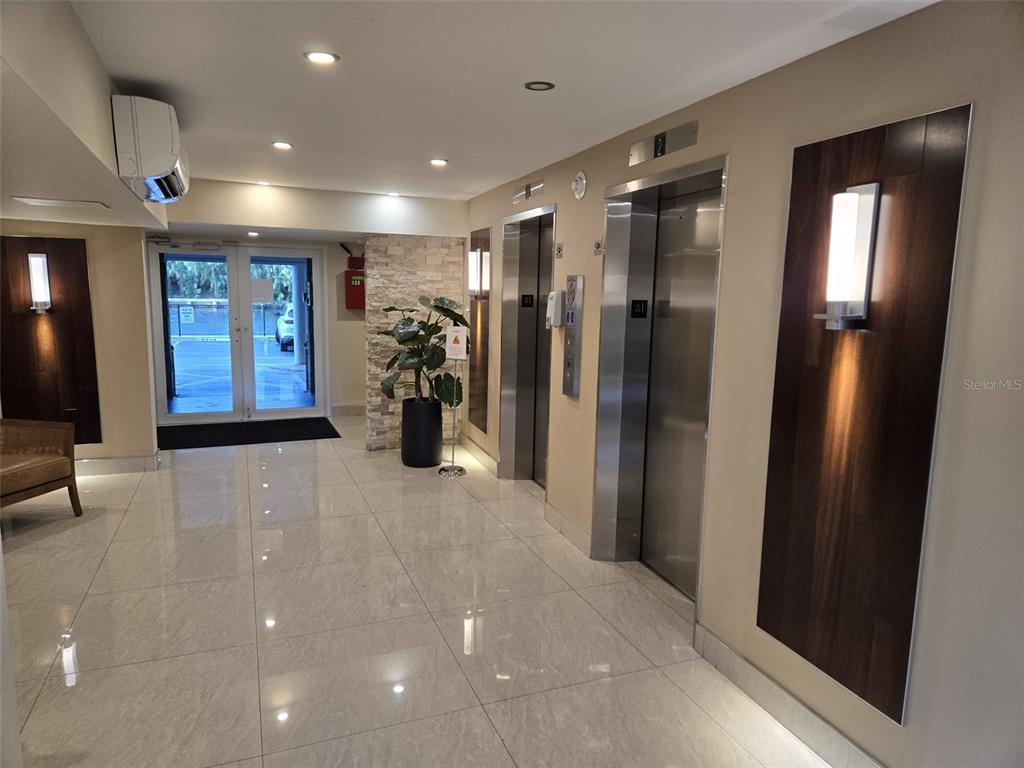 A modern building lobby features tiled floors, two stainless steel elevators, and glass entry doors — 300 DIPLOMAT PARKWAY UNIT 203, HALLANDALE BEACH, FL