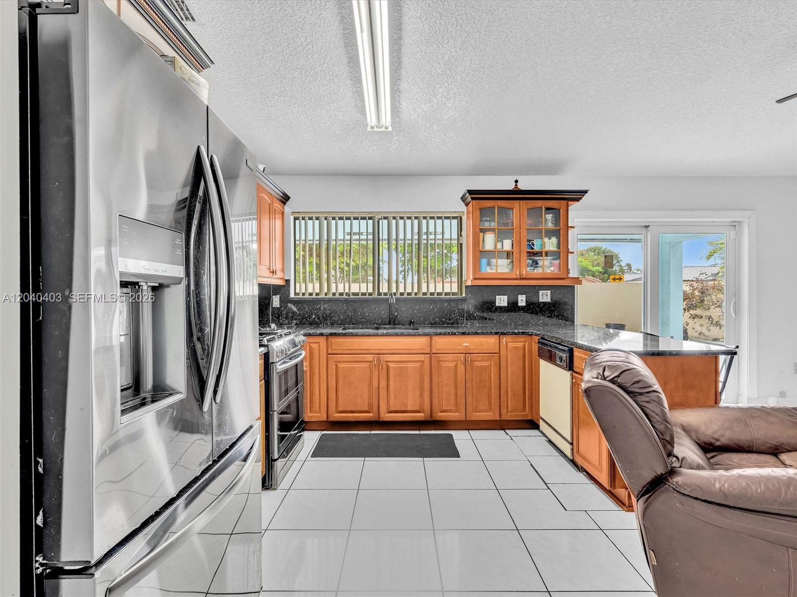 A kitchen features wood cabinets, black countertops, stainless steel appliances, and white tile flooring — 16951 SW 147th Ct, Miami FL 33187, MIAMI, FL