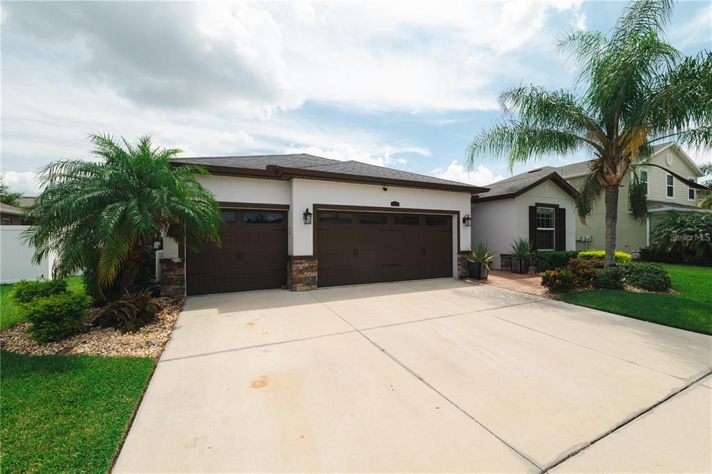 A single-story house with a three-car garage and palm trees in the front yard — 5635 FISHER GLEN LOOP, WESLEY CHAPEL, FL