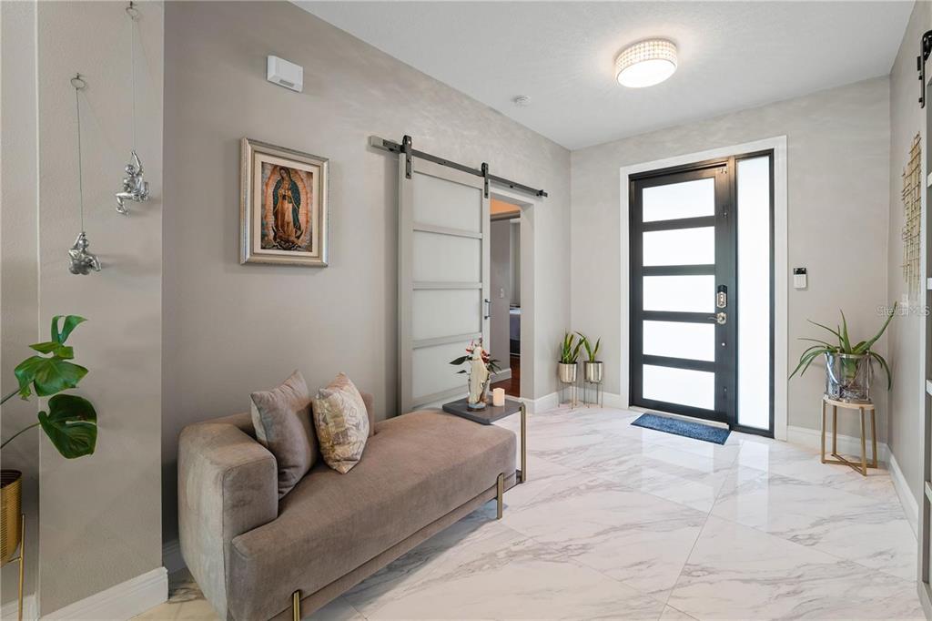 A modern entryway features marble tile floors, a gray chaise lounge, and a sliding barn door — 5635 FISHER GLEN LOOP, WESLEY CHAPEL, FL