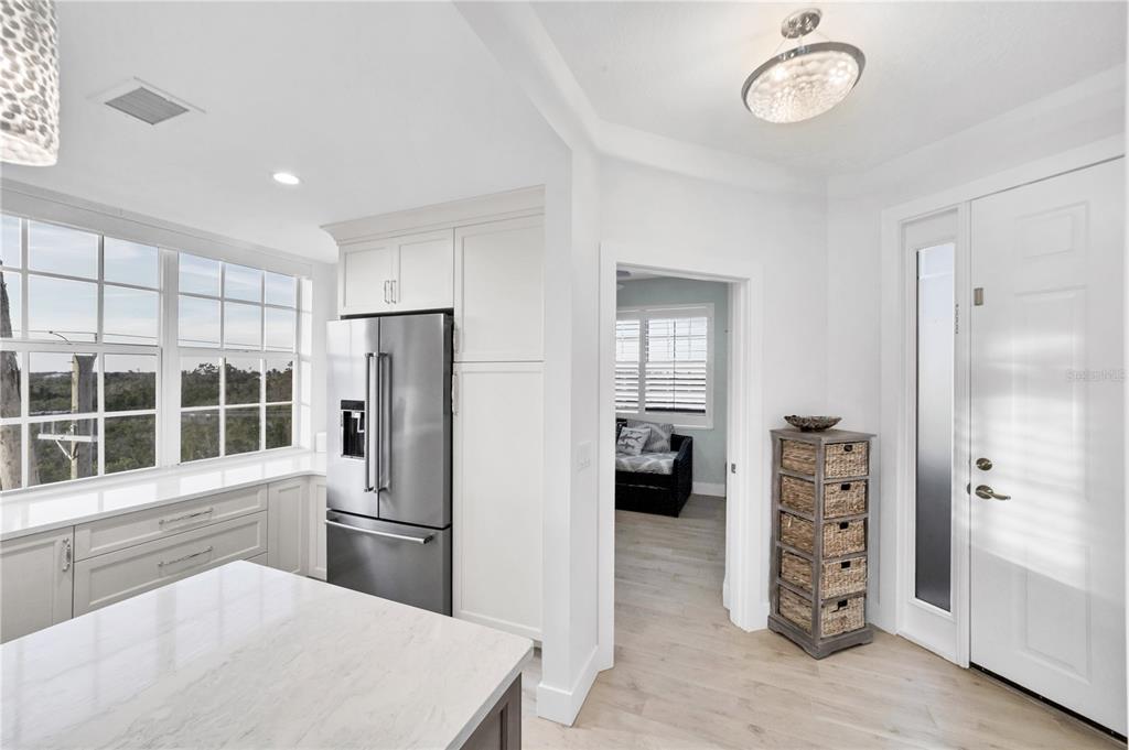 A bright kitchen features white cabinetry, a stainless steel refrigerator, and a view of trees — 13113 GASPARILLA ROAD UNIT 405, PLACIDA, FL