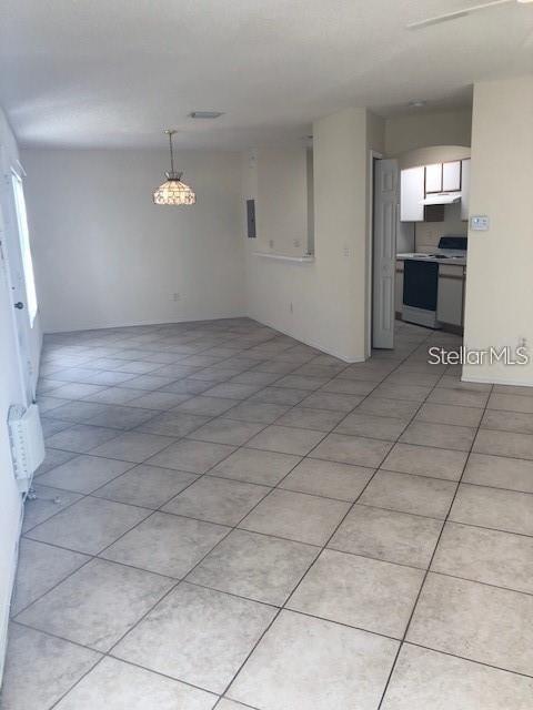 An open-concept living area features light-colored tile flooring and a view into a small kitchen — 1735 FLUORSHIRE DRIVE, BRANDON, FL