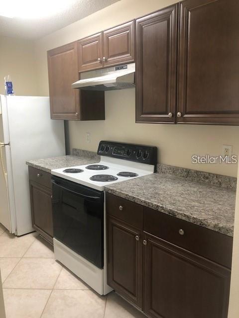 A kitchen features dark wood cabinets, a white electric stove, and speckled laminate countertops — 1735 FLUORSHIRE DRIVE, BRANDON, FL