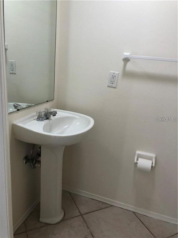 A small bathroom features a white pedestal sink, a wall mirror, and a toilet paper holder — 1735 FLUORSHIRE DRIVE, BRANDON, FL