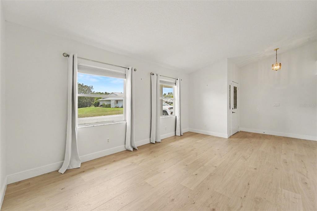An empty room features light wood-look flooring, white walls, and two windows with curtains — 26166 NEWCOMBE CIR, LEESBURG, FL