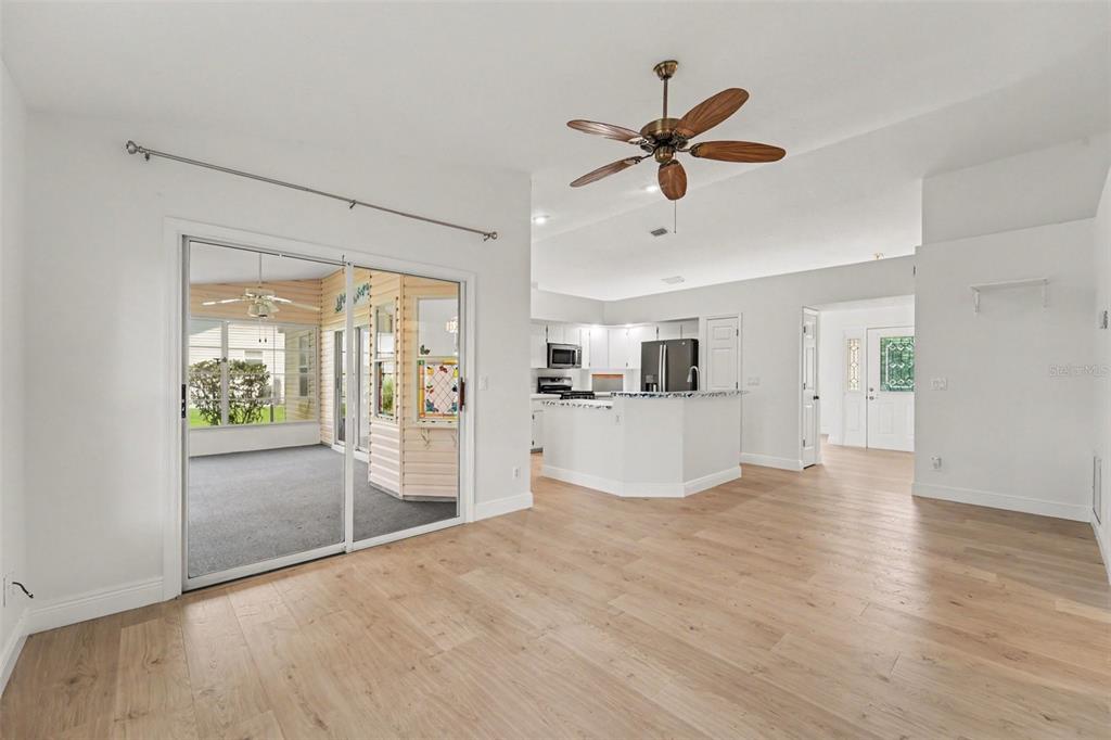 A bright living room with light wood floors, a ceiling fan, and sliding glass doors — 26166 NEWCOMBE CIR, LEESBURG, FL