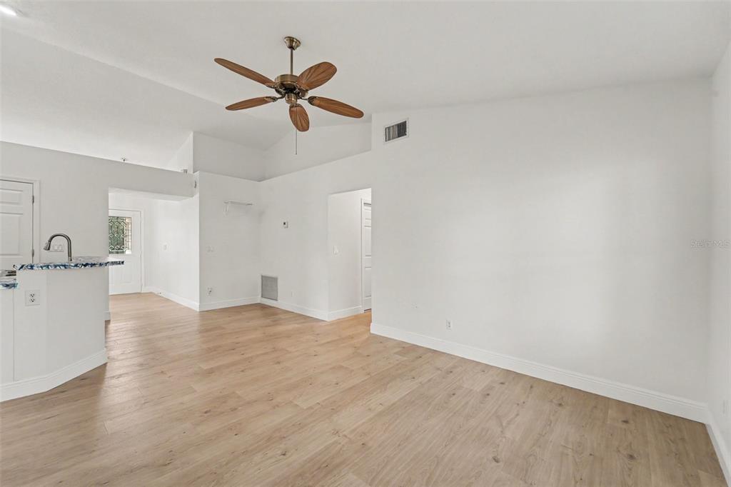 An empty living room features light wood-look flooring, white walls, and a ceiling fan — 26166 NEWCOMBE CIR, LEESBURG, FL