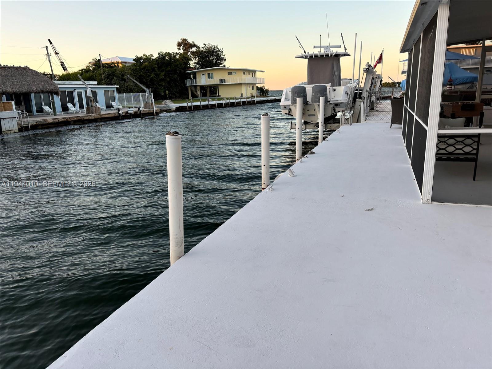A white dock extends over the water toward a boat and waterfront houses — 235 Anne Bonny Dr, Key Largo FL 33037, KEY LARGO, FL