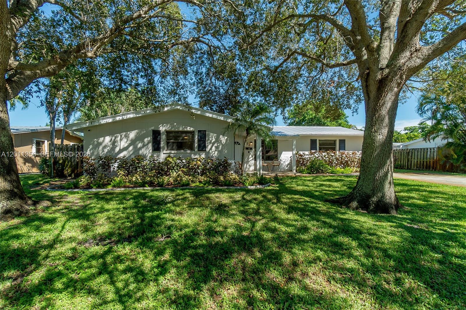 A single-story house with a light-colored exterior sits behind large trees on a grassy lawn — 712 Tradewind Dr, North Palm Beach FL 33408, NORTH PALM BEACH, FL