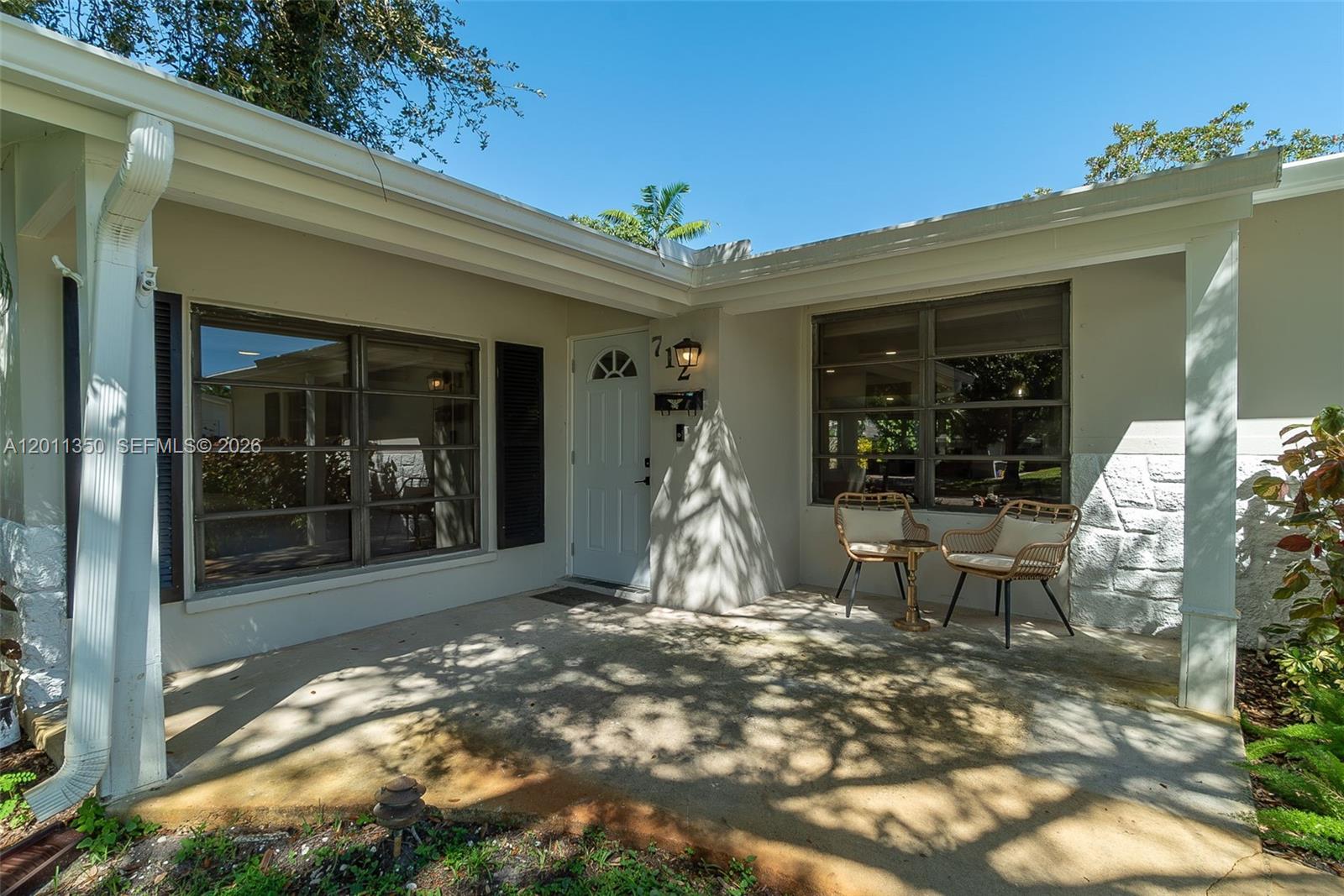 A concrete porch features two wicker chairs and a small table in front of a house — 712 Tradewind Dr, North Palm Beach FL 33408, NORTH PALM BEACH, FL