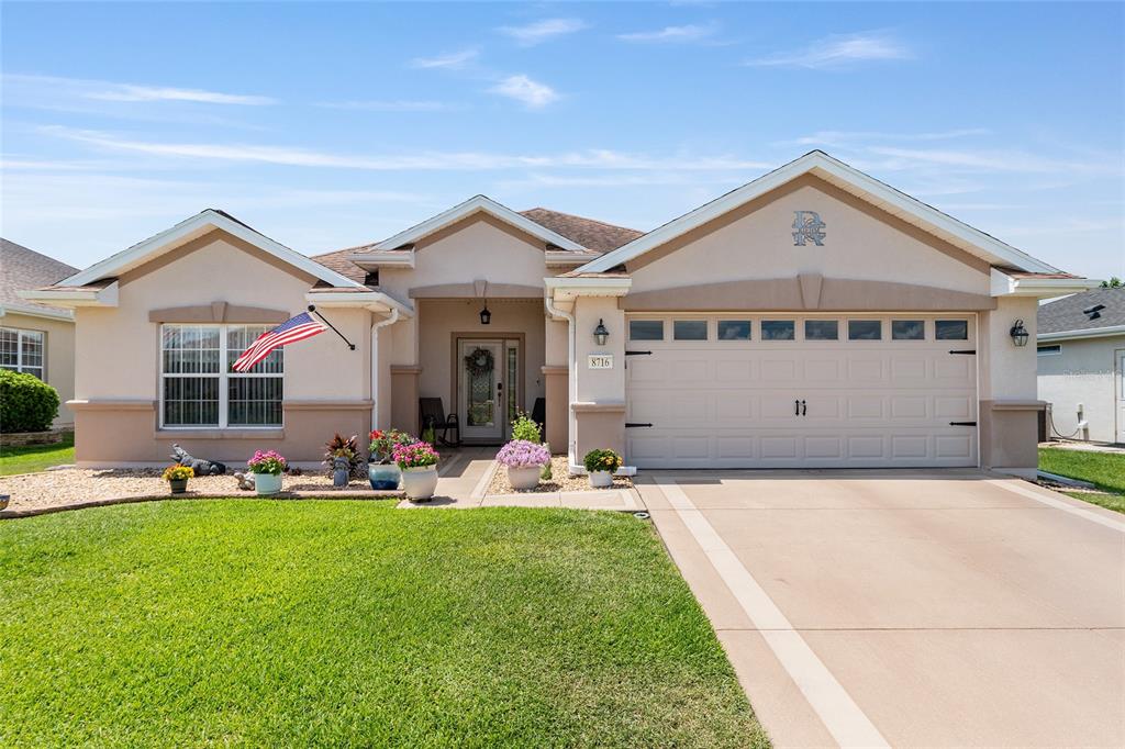 A single-story suburban house with a beige stucco exterior, a two-car garage, and landscaping — 8716 SE 136TH PLACE, SUMMERFIELD, FL