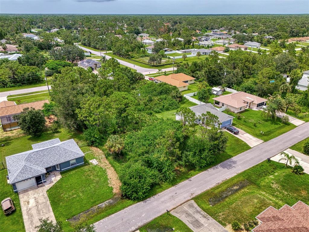 An aerial view shows a vacant, tree-covered lot situated between several single-family homes — DUAR TERRACE, NORTH PORT, FL