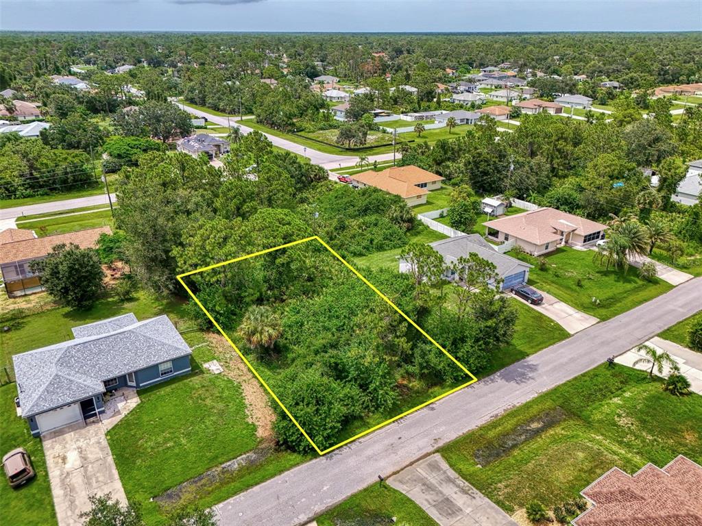 An aerial view shows a vacant, wooded residential lot outlined in yellow between two houses — DUAR TERRACE, NORTH PORT, FL