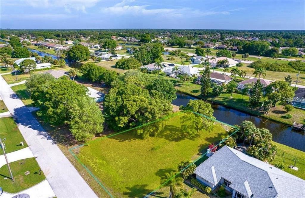 An aerial view shows a vacant, grassy residential lot bordered by a canal and trees — 74 MARINER LANE, ROTONDA WEST, FL