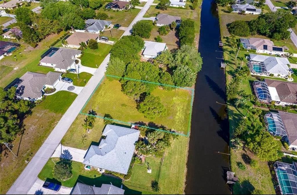 An aerial view shows a vacant, tree-covered residential lot situated between a road and a canal — 74 MARINER LANE, ROTONDA WEST, FL