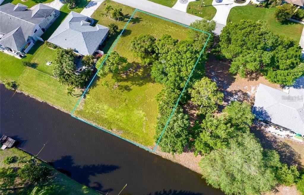 An aerial view shows a vacant, tree-lined residential lot situated along a canal — 74 MARINER LANE, ROTONDA WEST, FL