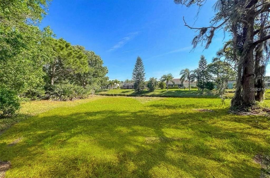 A grassy lot features mature trees and a small canal under a clear blue sky — 74 MARINER LANE, ROTONDA WEST, FL