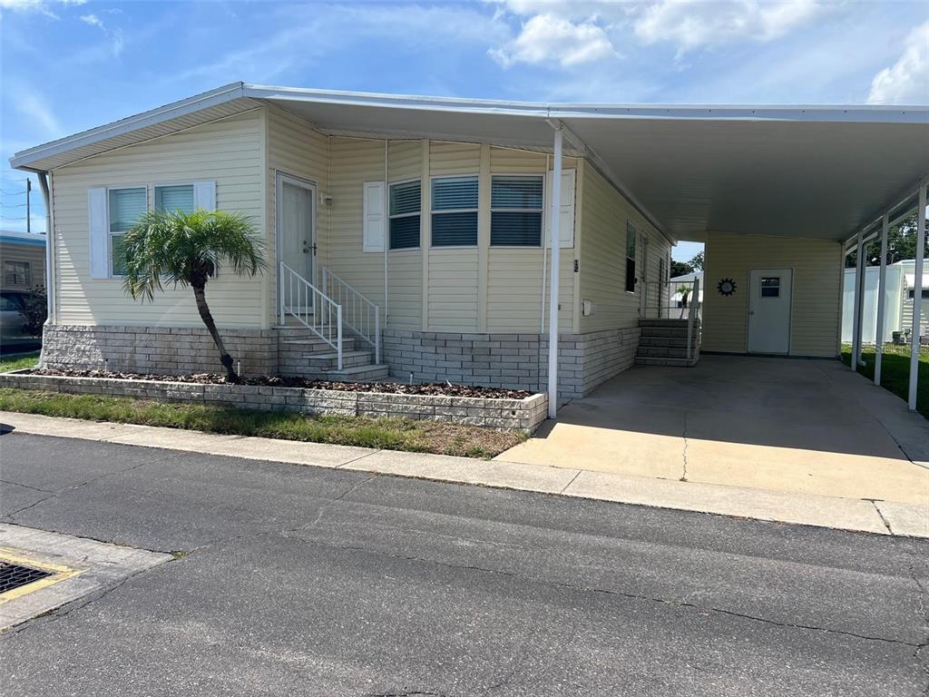 A light yellow manufactured home features a brick-faced base, a carport, and a small palm tree — 12 THATCH PALM STREET W, LARGO, FL
