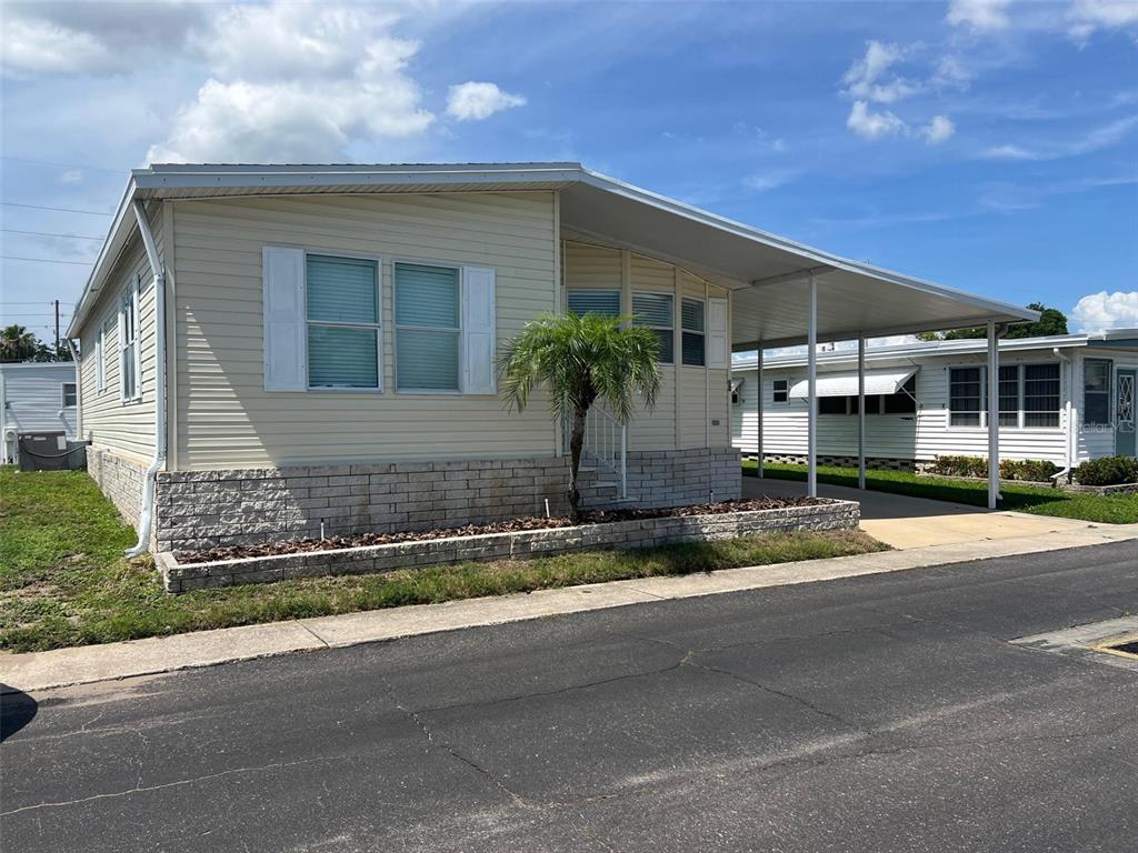 A light-colored mobile home features a stone-veneer base, a carport, and a small palm tree — 12 THATCH PALM STREET W, LARGO, FL