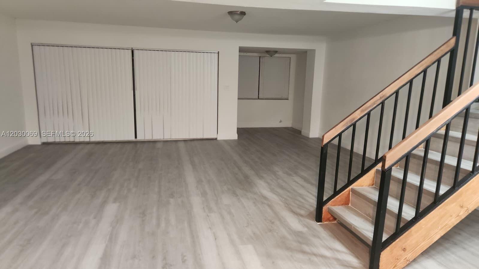 A room with light wood-look flooring, white walls, vertical blinds, and a wooden staircase — 1817 NW 58th Ave # 22, Lauderhill FL 33313, LAUDERHILL, FL