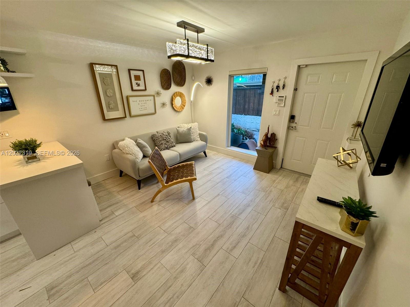 A living room features light wood-look tile flooring, a gray sofa, and a modern chandelier — 1121 SW 7th St # 1, Miami FL 33130, MIAMI, FL