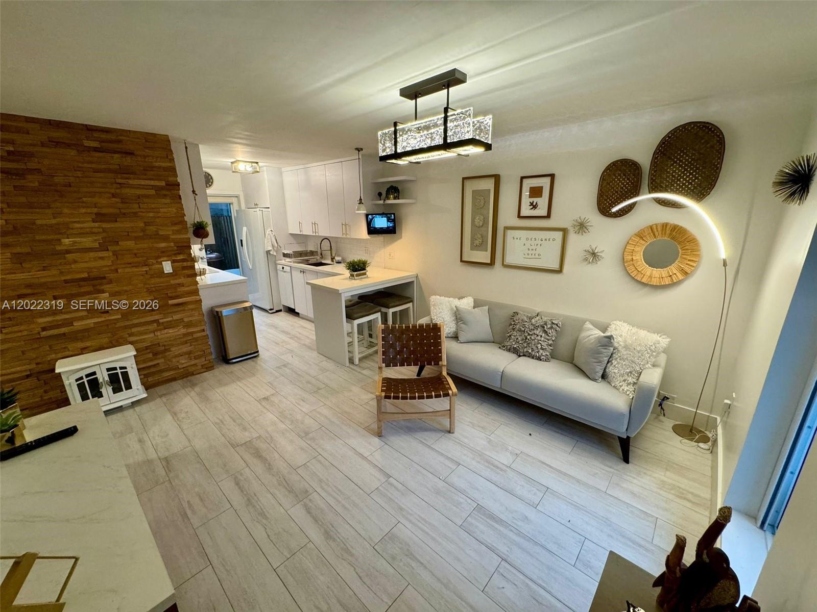 A living room features a light gray sofa, wood-slat accent wall, and an open kitchen — 1121 SW 7th St # 1, Miami FL 33130, MIAMI, FL